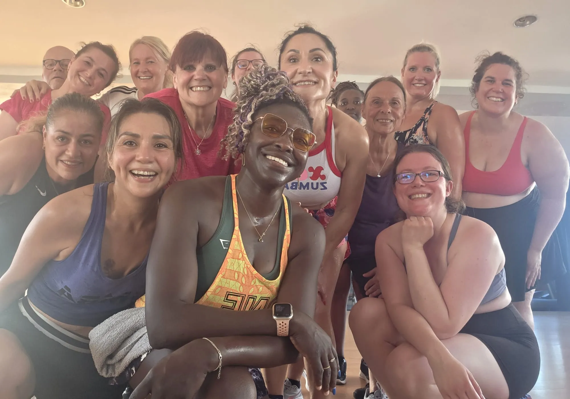 Lachende Gruppe aus dem Zumba-Kurs, dicht beieinander im Kursraum